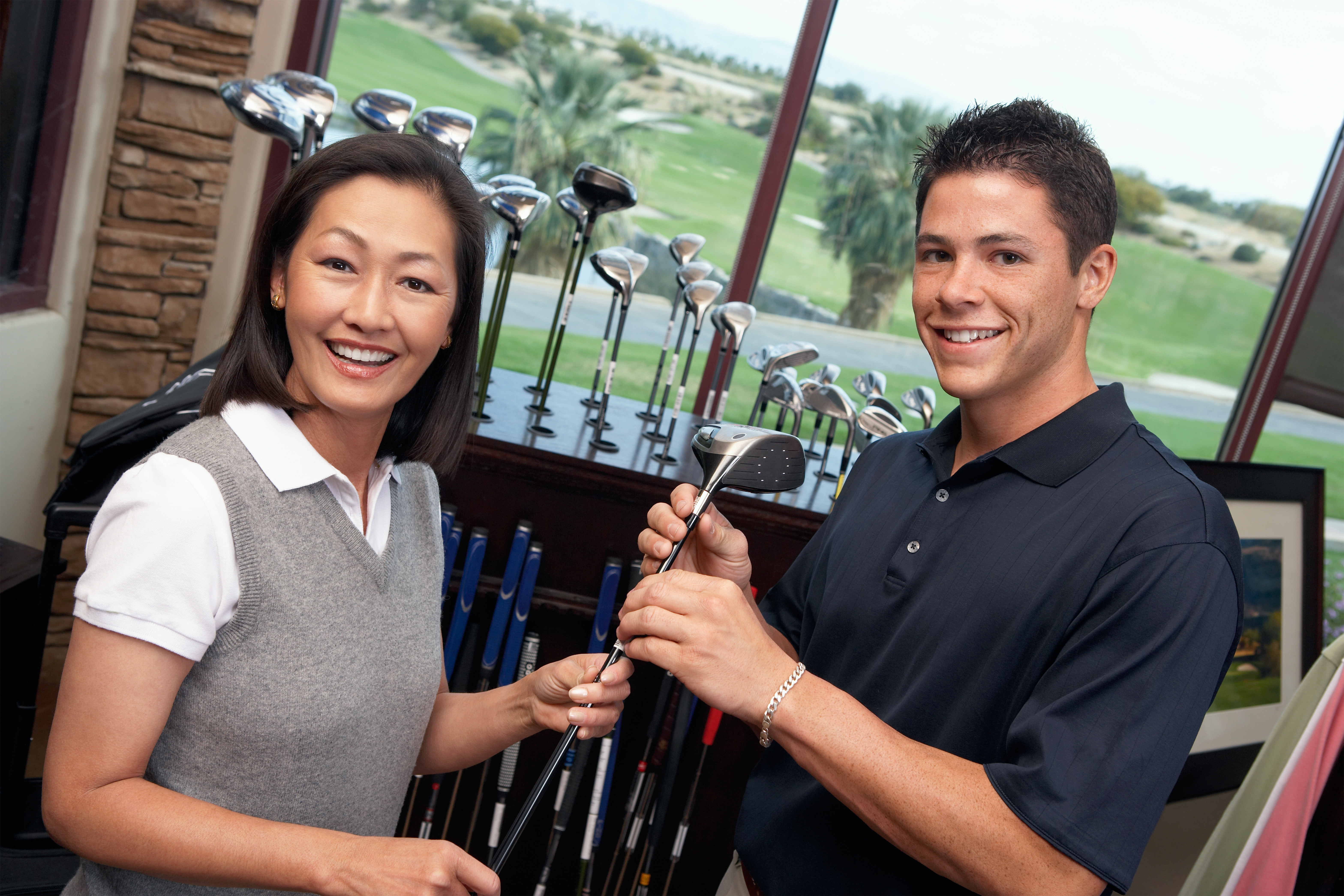 Smiling clerk assisting mid adult woman shopping for golf clubs in golf shop